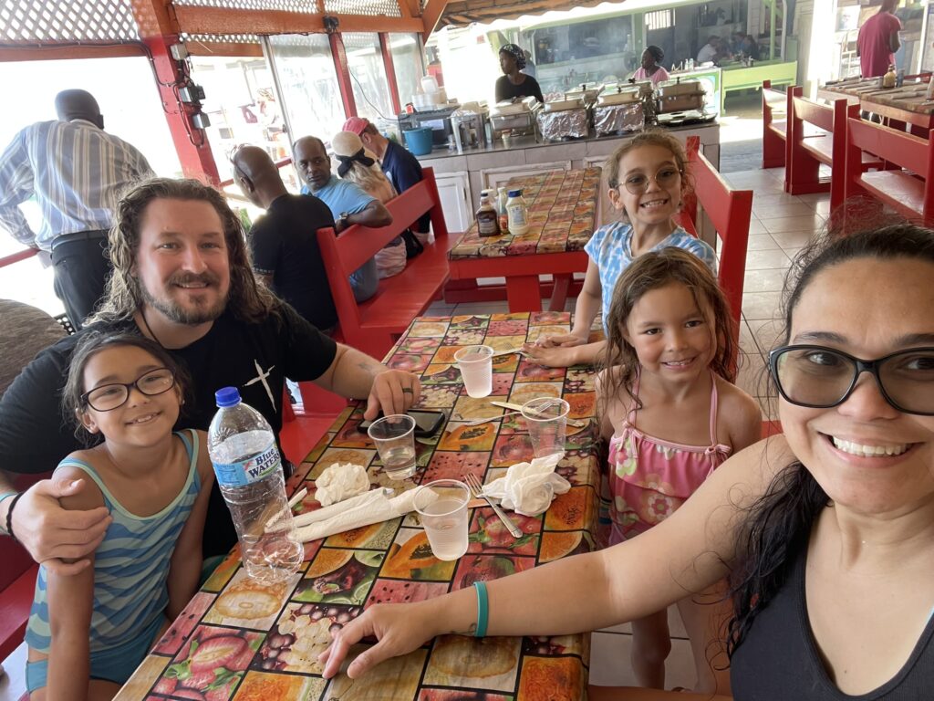 Family enjoying French Caribbean Creole cuisine at The LoLos in Saint Martin — smiling selfie at a busy open-air restaurant after a Caribbean swim.