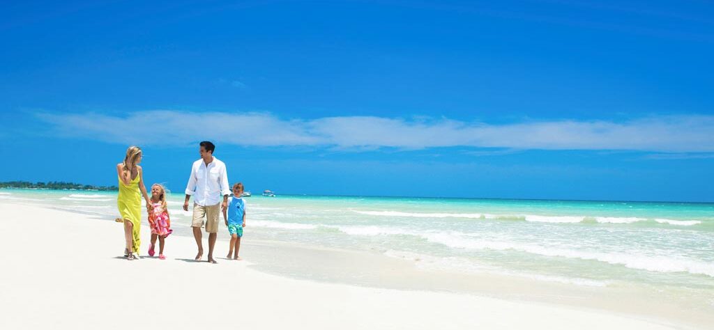 Family walking along a white sand beach with turquoise water, representing all-inclusive family vacation packages.
