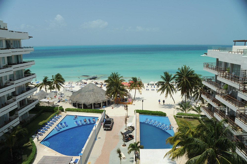 View of IXCHEL hotel, Isla Mujeres, Mexico, beach access and pool from penthouse balcony, showing the shallow, calm turquoise Caribbean Ocean all around it.