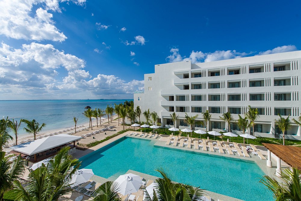 View of Izla hotel, Isla Mujeres, Mexico, beach access and pool from mid-level corner balcony, showing the expansive, calm turquoise Caribbean Ocean extending into the horizon.
