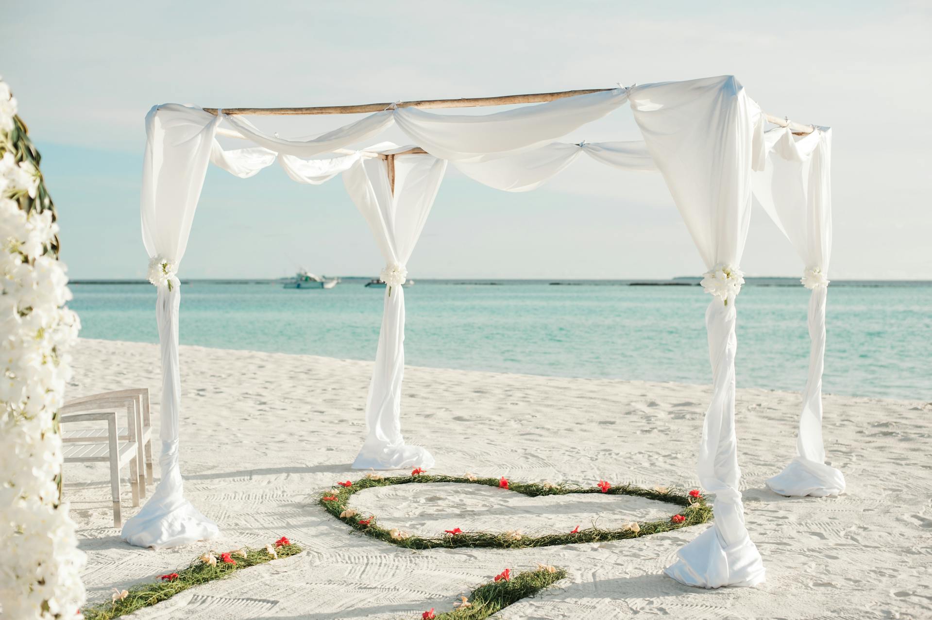 Wedding arch draped in white linen and flowers on the beach in the Maldives, perfect for all-inclusive destination weddings and honeymoons.