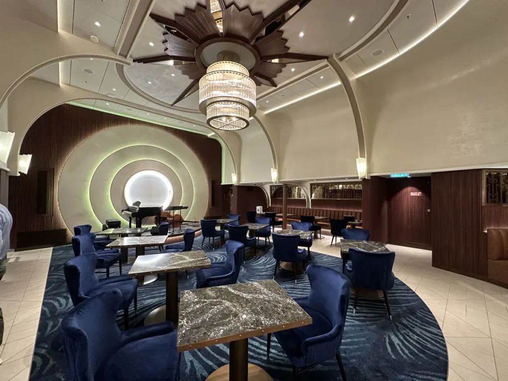 Image of the Icon ship classes Empire Supper Club dining room layout with its main chandelier over the table and chairs against the backdrop of the orchestra area representing an upscale, all-inclusive, fine dining elegance for your luxury cruise dream vacation.