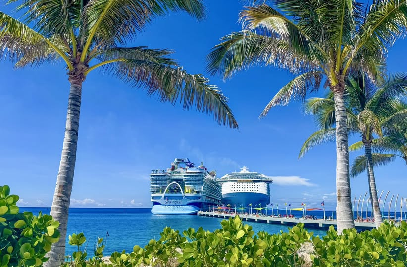 View of two Royal Caribbean Icon class ships docked at their private island Perfect Day at CocoCay, from the island shoreline with palm trees and turquoise lagoon which is a must-see stop when you cruise into your dream vacation.