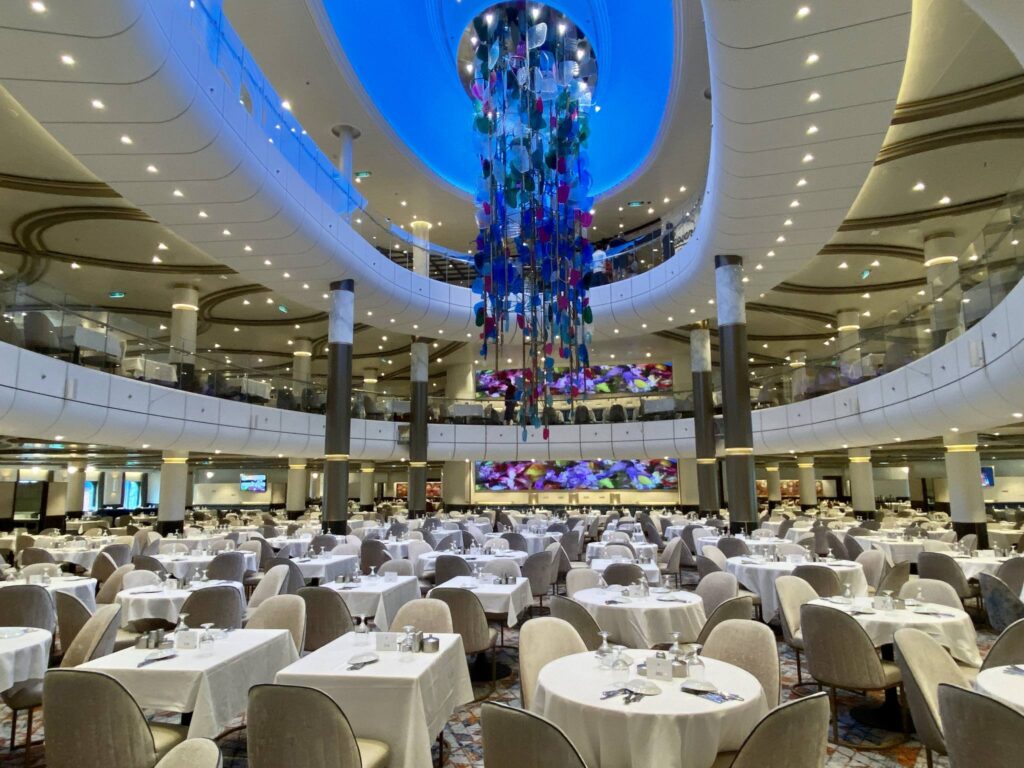 Royal Caribbean Icon of the Seas grand main dining hall with its three levels and its ceiling to mid-level hanging centerpiece resembling the tentacles of a jellyfish shows the vast amounts of space this ship has for serving its guests and the quality of its decor, furniture and tablescapes set for you to cruise into your dream vacation.