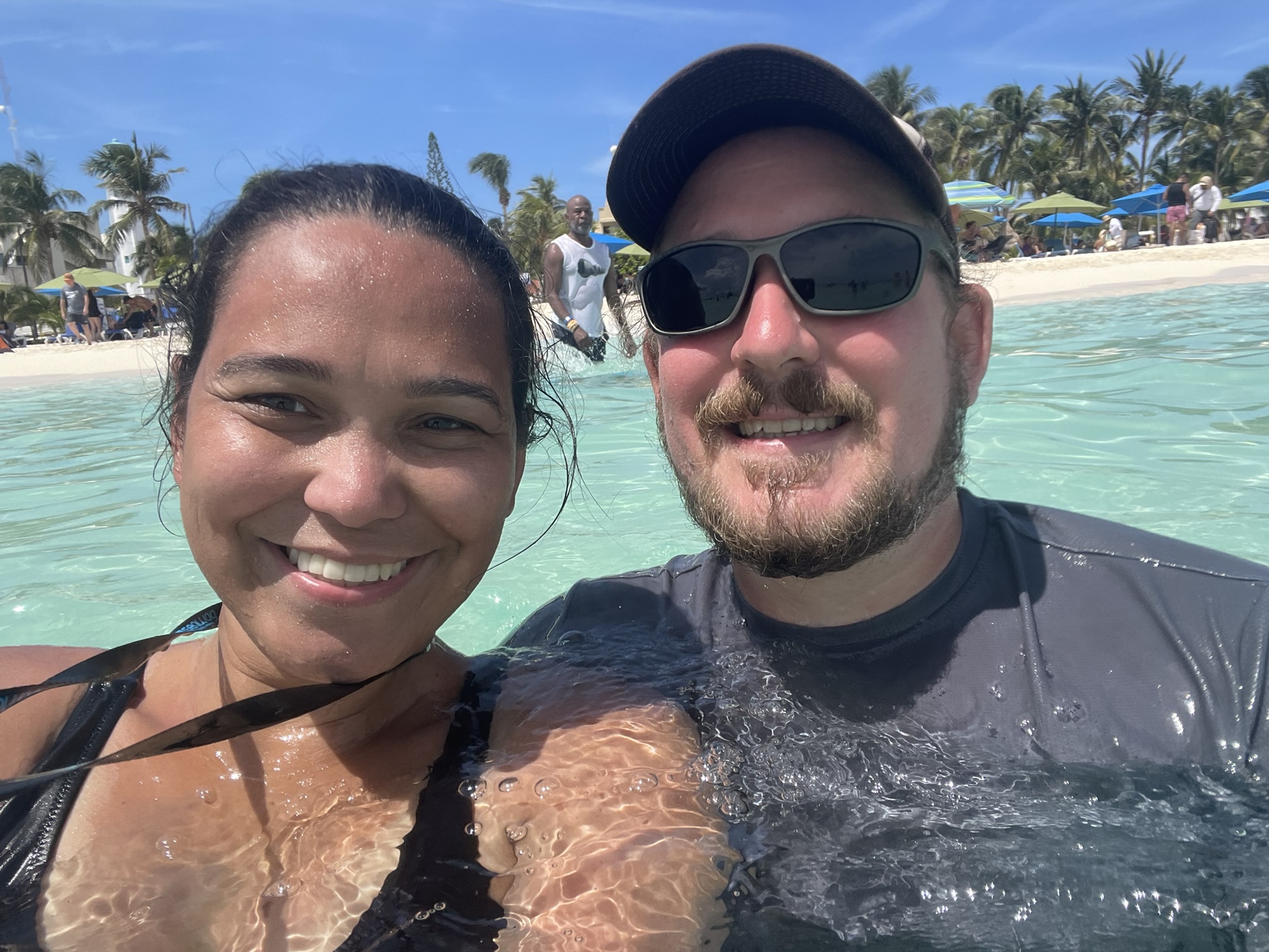 Couple smiling for a selfie while wading in the warm, crystal-clear waters of Playa Centro on Isla Mujeres, Mexico.