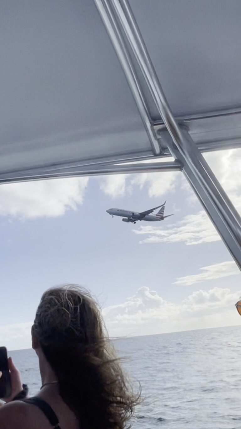 American Airlines plane flying low over an Anguilla speedboat tour right off Maho Beach as it lands at Princess Juliana Airport in Saint Martin.