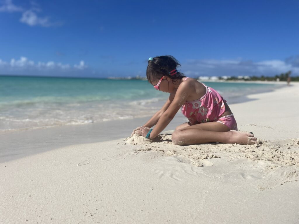 Child building a small sand creation on the beach at Rendezvous Bay Anguilla with the turquoise Caribbean shoreline softly blurred behind.