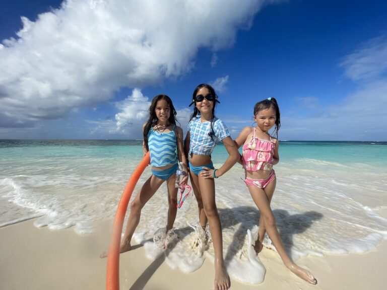 Three children standing in the shoreline at Shoal Bay Anguilla looking out toward the deep blue Caribbean horizon.