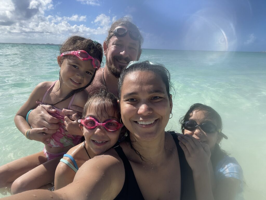 Family smiling together while standing in waist deep crystal-clear water at Rendezvous Bay Anguilla.