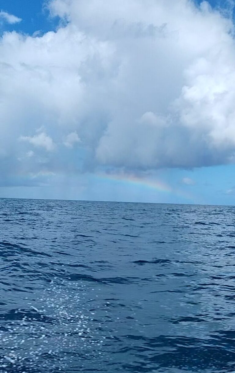 Rainbow stretching across the Caribbean Sea during a Saint Martin to Anguilla speedboat tour with deep blue water and sea spray along the boat railing.