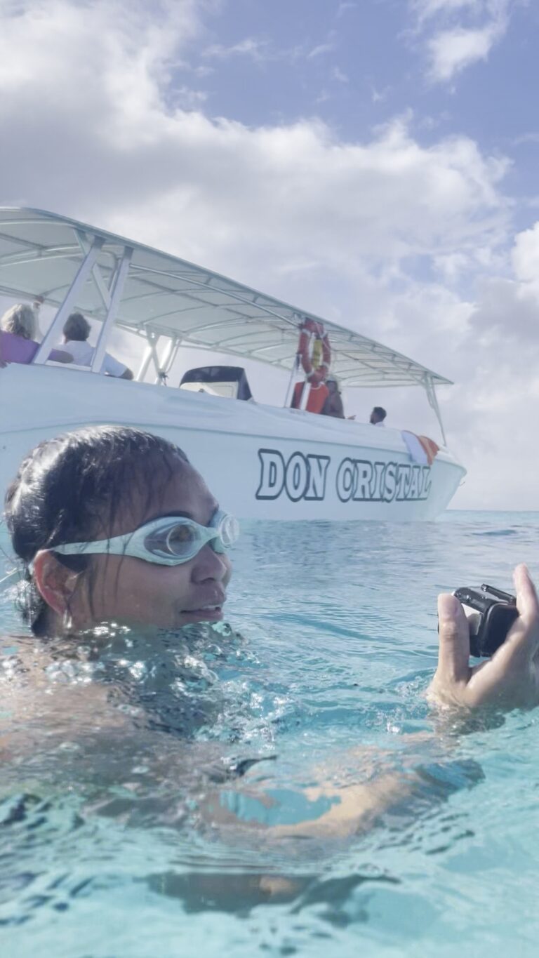 Traveler holding a recovered GoPro camera found on the ocean floor in crystal clear water at Meads Bay Anguilla with speedboat tour boat in background.